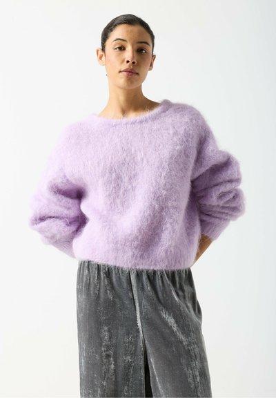 Pull en mohair lilas avec de larges poignets et une coupe décontractée, associé à une longue jupe en velours gris avec une fente latérale.