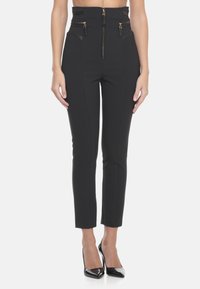 Pantaloni neri a vita alta in un materiale elastico con dettagli in zip dorati, lunghezza cropped e vestibilità sartoriale.