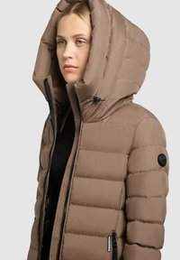 Hnedá zateplená bunda s veľkou kapucňou, prešívaná textúra, čierne akcenty a zips na prednej strane. Má bočnú kapsu a detail s logom.