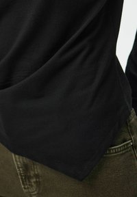 Μαύρο υφασμάτινο πουκάμισο που καλύπτει το πάνω μέρος ελαφρώς πράσινου τζιν παντελονιού με ορατές τσέπες και ραφές.