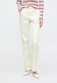 Hvide bomuldsbukser med vide ben, forlommer og høj talje, kombineret med en rød- og hvidstribet langærmet top og beige sko.