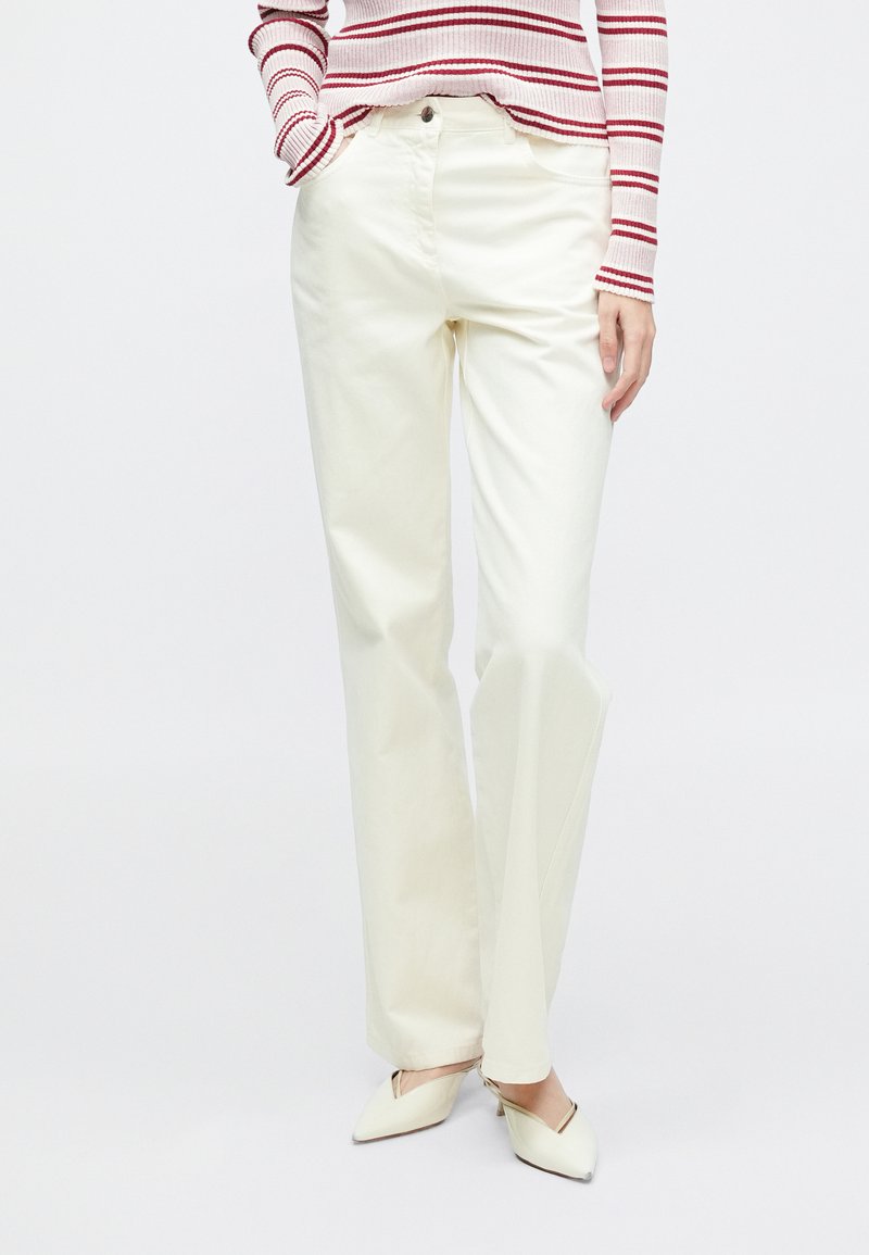 Hvide bomuldsbukser med vide ben, forlommer og høj talje, kombineret med en rød- og hvidstribet langærmet top og beige sko.