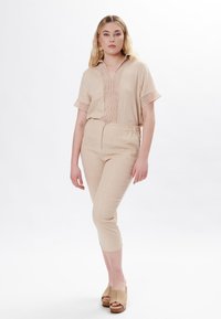Blusa di lino beige con maniche corte e scollatura a V, caratterizzata da ricami verticali. Pantaloni affusolati abbinati, anch'essi beige, con una cintura elastica.
