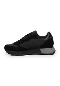 Sneaker bassi neri con pannelli in rete e suede, lacci neri e una spessa suola in gomma grigia e nera, mostrati di lato su sfondo bianco.