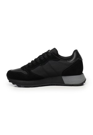 Sneaker bassi neri con pannelli in rete e suede, lacci neri e una spessa suola in gomma grigia e nera, mostrati di lato su sfondo bianco.