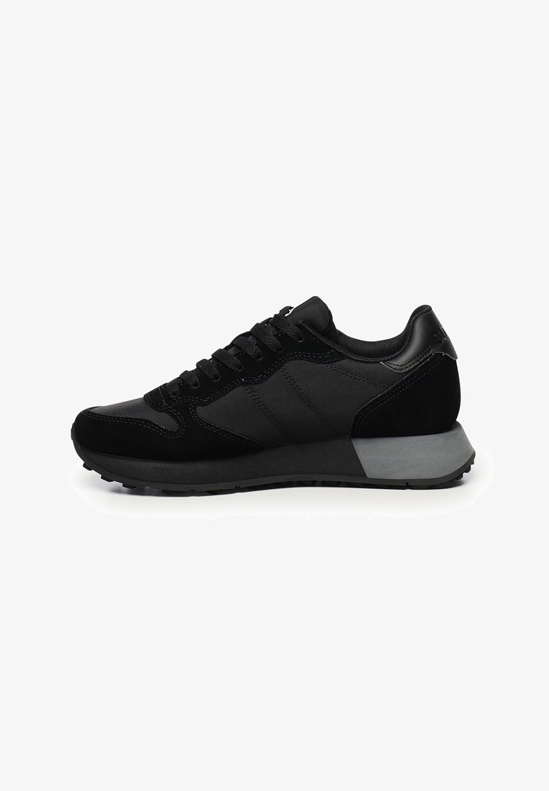 Sneaker bassi neri con pannelli in rete e suede, lacci neri e una spessa suola in gomma grigia e nera, mostrati di lato su sfondo bianco.