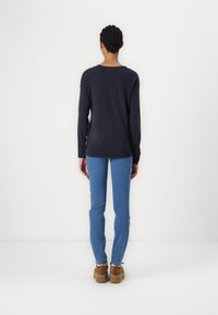 Pull-over en maille bleu marine à manches longues avec une coupe décontractée, associé à un jean bleu clair et des chaussures compensées marron. Design simple, texture douce.