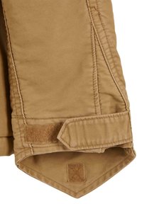 Pantalones de algodón color beige con dobladillo ajustado, que presentan un parche de velcro y detalles de costura a lo largo de las costuras.