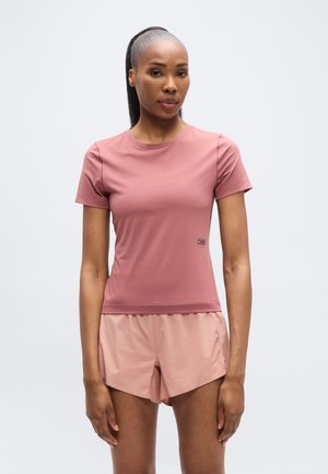 Lühikeste varrukatega, ümar kaelusega roosa sportliku top, mida on kombineeritud sobivate roosade lühikestega, millel on peen logo ja kerge, sile kangas.