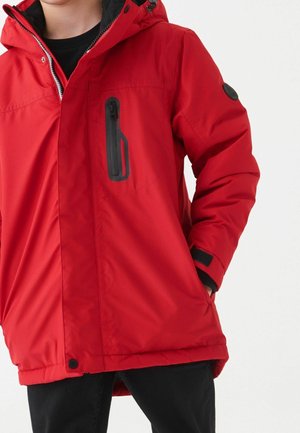 Červená izolační bunda se zipovou náprsní kapsou, černými akcenty, nastavitelnou kapucí a suchými zipy na manžetách. Hladká textura, délka do kolen.