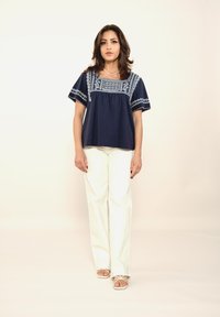 Haut bleu marine avec des détails brodés autour de l'encolure et des manches courtes, associé à un pantalon large blanc et des sandales à lanières.