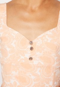 Bluzka z materiału w brzoskwiniowy wzór, z kwadratowym dekoltem, ozdobiona trzema guzikami i teksturowanym wzorem paisley. Gładka powierzchnia.