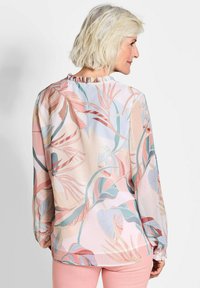 Leichte, pastellfarbene Bluse mit langen Ärmeln, gerafftem Rüschenausschnitt und dezenten Blättermustern in zarten Rosa-, Grün- und Blautönen.