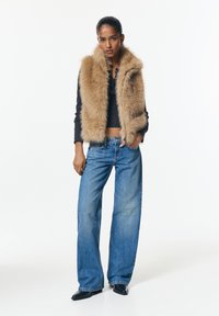 Könnyűbarna műszőrme mellény, magas gallérral. Széles szárú kék farmernadrággal és fekete bokacsizmával párosítva. Alatta egy egyszerű, testhezálló fekete felső.