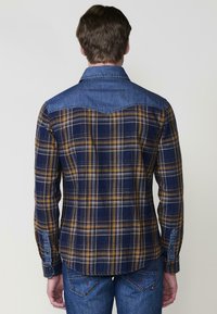 Kockás ing sötétkék, sárga és fehér színben, farmer yoke-kkal és gallérral. Hosszú ujjú, gombos mandzsettával, hátul ívelt hem-mel.