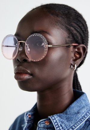 Runde solbriller med rosa gradientlinser, prydet med sølvnagler langs rammen, festet til tynne metallarmer.