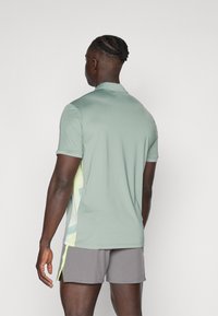Light green short-sleeve polo shirt with collar; features geometric accents in yellow and blue on the side; paired with gray shorts.