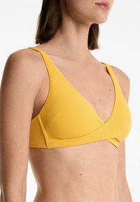 Sostenitore triangolare in tessuto a coste giallo con spalline larghe e scollatura a V profonda. Presenta un design senza cuciture e un dettaglio con cucitura anteriore invertita.