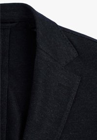 Blazer gris oscuro con solapa de muesca, tejido texturizado y un bolsillo oculto. Vista en primer plano que destaca los detalles del cuello y la solapa.