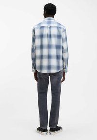 Geruit overhemd in lichtblauw en wit, zachte stof, lange mouwen met knoopmanchetten, detail op het rugpand, gedragen met grijze spijkerbroek en zwarte sneakers.