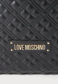 Black quilted leather surface with gold metal plate reading "LOVE MOSCHINO" attached by four gold rivets.