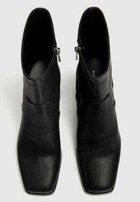 Bottes basses en cuir noir avec un bout carré, une texture lisse, une fermeture éclair et un design élégant. La tige présente des lignes de contour subtiles.