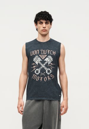 Jeune homme aux cheveux bouclés et foncés portant un débardeur noir sans manches avec un motif de pistons croisés et le texte « Von Dutch Motors 1929 ».