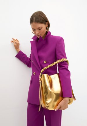 Blazer croisé de couleur violet vif, associé à un sac seau métallique doré avec une poignée tressée et une texture lisse.