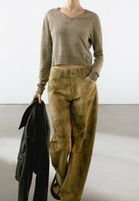 Pull marron court en tissu tricoté, associé à un pantalon en cuir beige ample avec une texture délavée et des poches avant. Tenant une veste en cuir noire.