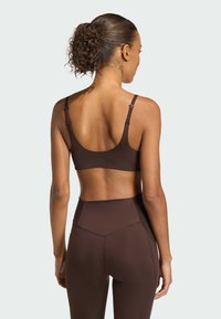Hnedá športová podprsenka so širokými ramienkami a bezšvovým dizajnom. Tkanina pôsobí hladko a elasticky, poskytujúc priliehavý strih.