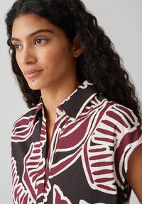 Camicia a maniche corte in bordeaux scuro e crema con audaci motivi a foglia, caratterizzata da un colletto classico e una texture morbida.
