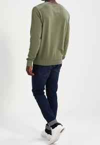 Olivgrön sweatshirt med ribbad nederkant och ärmslut, matchad med mörkblå jeans och vita sneakers med svarta detaljer. Bakifrån.