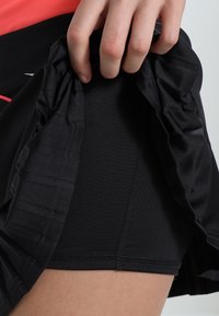 Svarta sportshorts i strukturerad tyg, med resårmidja och sidoklyv för förbättrad rörlighet. Accenterade med röda sömmar.
