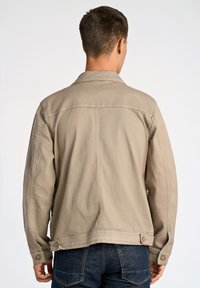 Beige denimjacka med knappad krage, sidfickor och en avslappnad passform. Har sömdetaljer och justerbara manschettknappar.