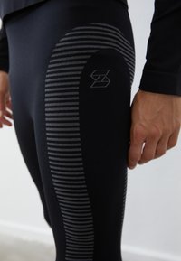 Svarta atletiska leggings med ett texturerat randmönster på låret och en logotyp, med en figursydd design och en jämn tygtextur.