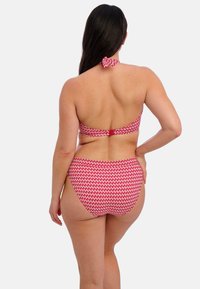 Bikini set s červeným a bílým vzorem, zahrnující top s krkem na šňůrku a kalhotky s středním páskem, prezentující hladký materiál a ozdobu v podobě mašle.