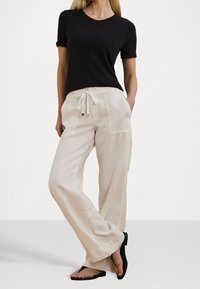 Svart kortärmad T-shirt, krämfärgade vida linnbyxor med dragsko i midjan och svarta flip-flops, mot en neutral bakgrund.