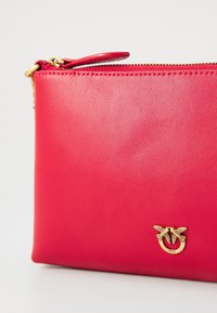 Borsa di pelle rossa con superficie testurizzata, caratterizzata da un accento ad anello dorato e chiusura a zip nella parte superiore per una conservazione sicura.