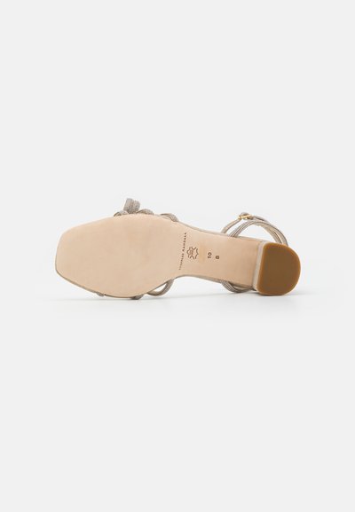 Sandale à talon haut beige avec des brides tressées, bout ouvert et semelle beige lisse. Équipée d'une boucle dorée pour le réglage.