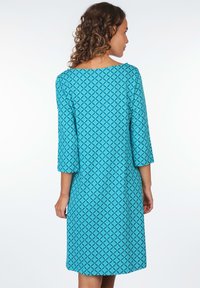 Türkises Kleid mit Dreiviertelärmel und geometrischem Muster. Glatte Textur, knielang, mit einem weit geschnittenen, runden Ausschnitt.