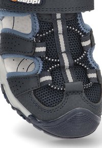 Sandal infantil azul marino con paneles de malla, correas de Velcro y suela de goma. Presenta acentos a rayas en gris y blanco y detalles perforados.