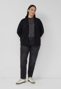 Czarny kardigan na szarym topie w panterkę, zestawiony z ciemnymi dżinsami i białymi trampkami. Charakteryzuje się luźnym krojem i teksturowanymi tkaninami.