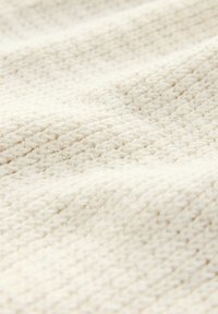 Krémově zbarvená pletenina s texturovaným, tkaným vzorem. Povrch vypadá jemně a útulně, s vyvýšenými stehy v konzistentním designu.