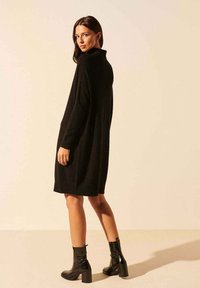 Robe noire en maille avec un col montant, des manches longues et une coupe ample, associée à des bottines noires à talon épais.