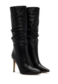 Botas de tobillo de cuero negro con punta afilada y tacón de aguja alto. La sección superior presenta detalles recogidos y drapeados para añadir textura.