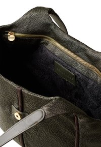 Green textured leather handbag with gold zipper, brown accents, and a dark interior featuring a logo patch and a zippered compartment.