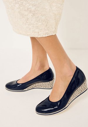 Chaussures compensées bleu marine avec une finition brillante, un bout arrondi et une semelle intermédiaire en tissage texturé avec des bordures blanches.
