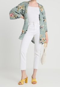 Floral kimono in light green fabric with oversized sleeves, worn over a white fitted top. White cropped jeans and yellow heeled sandals.