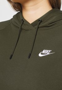 Sudadera verde con capucha hecha de tejido suave. Presenta un logo blanco de Nike en el pecho y puntas de cordón negras. Textura suave en toda la prenda.