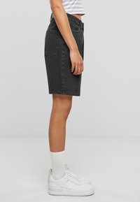 Pantalones cortos de mezclilla negra, hasta la rodilla, diseño de cinco bolsillos, dobladillo cosido, combinados con zapatillas blancas de caña alta y calcetines blancos de caña media.
